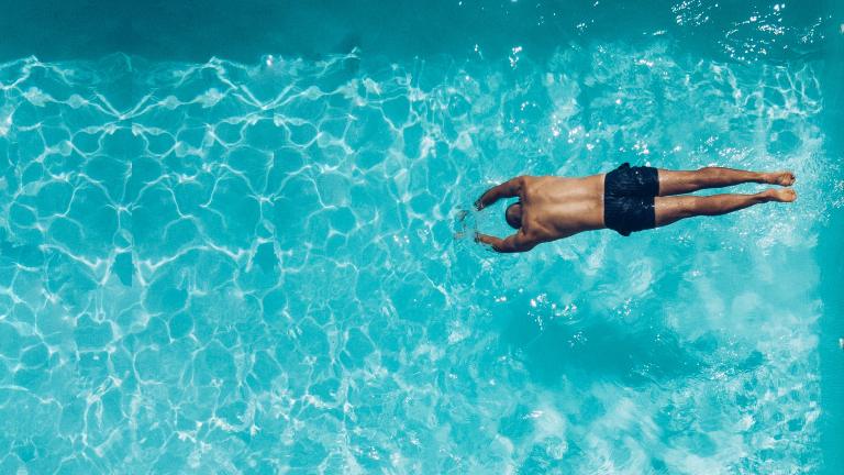 Ein Mann springt in einem Freibad kopfüber ins Wasser.