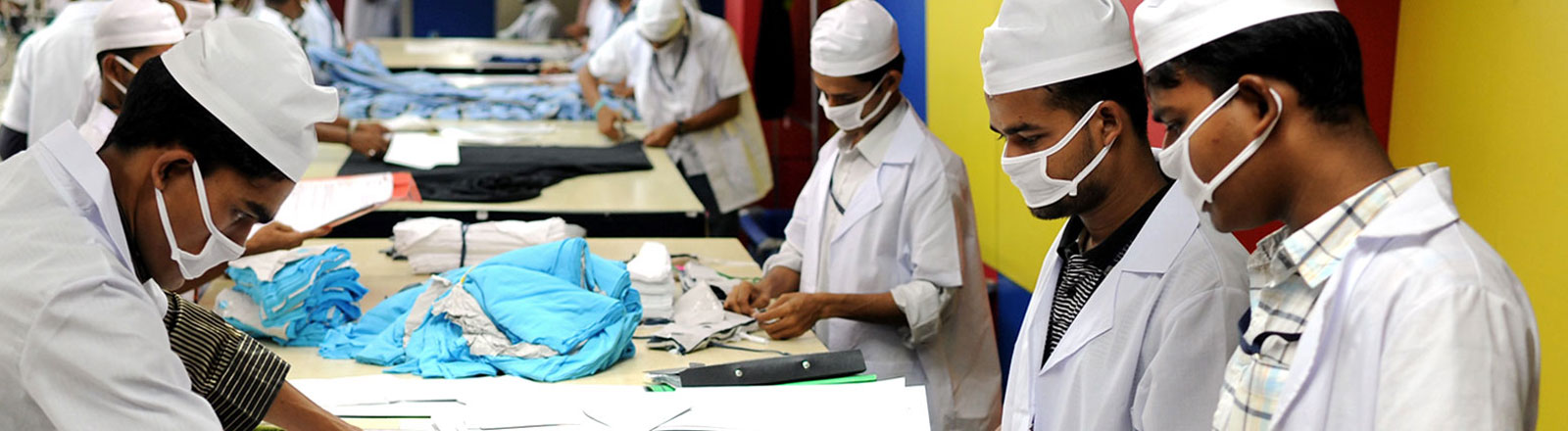 Arbeiter mit Mundschutz bei der Textilbearbeitung in Bangladesh
