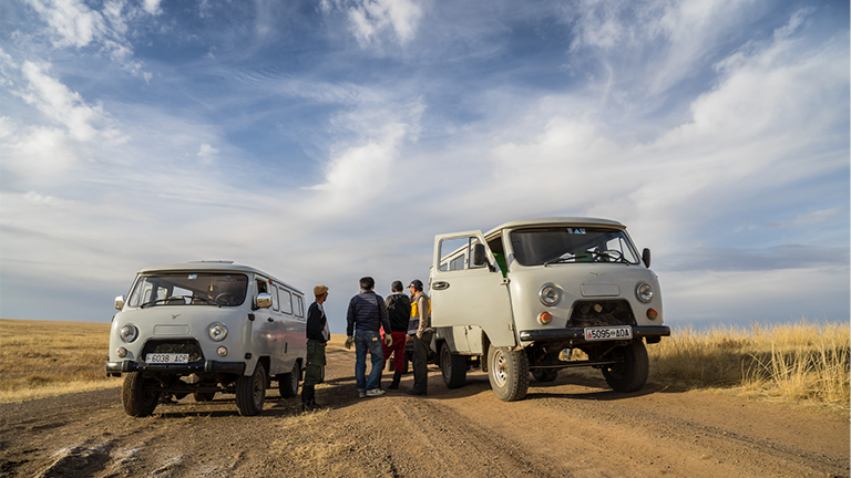 Zwei alte Lastwagen stehen in der mongolischen Steppe, daneben eine Gruppe von Menschen
