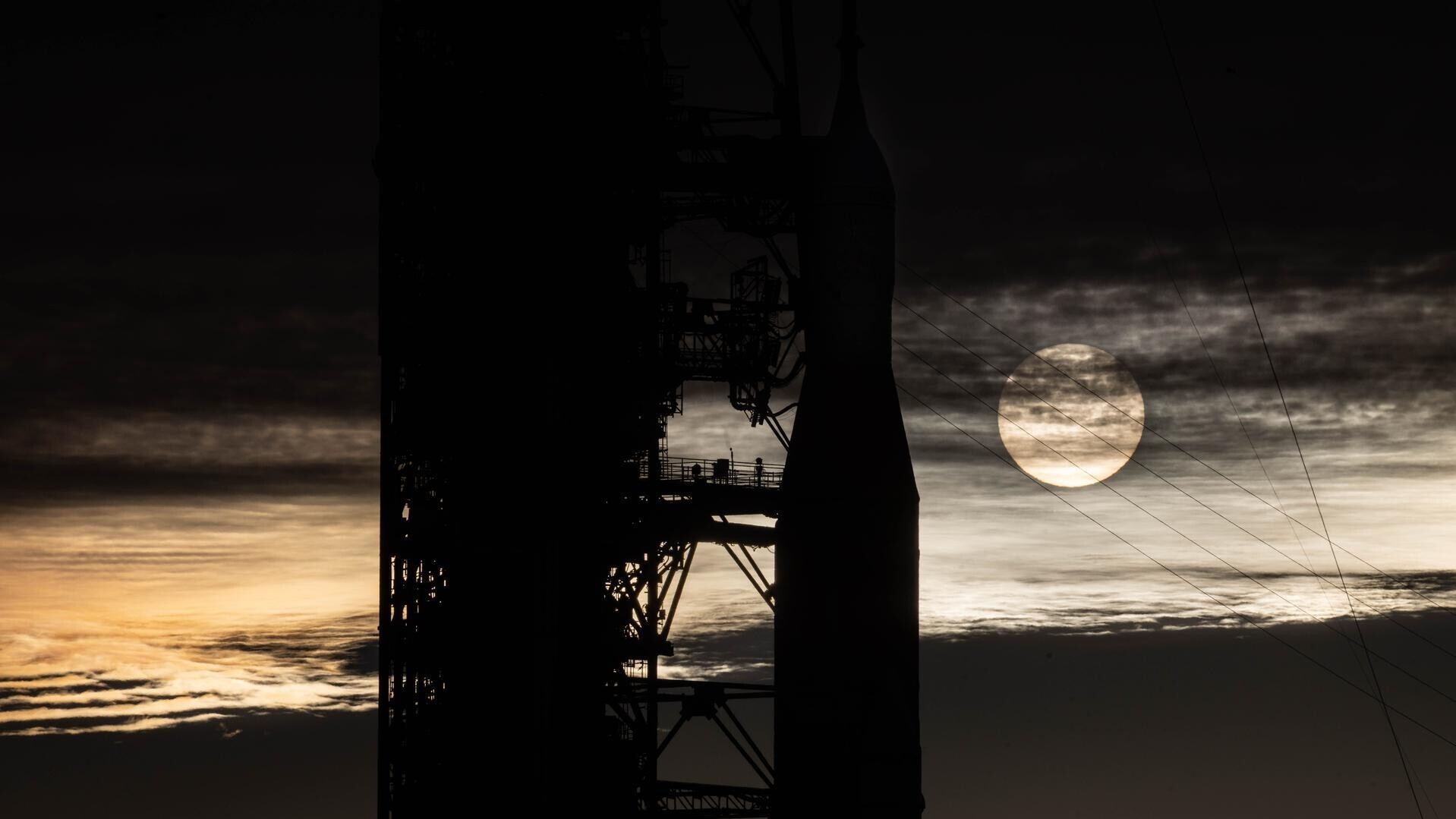 Sonnenaufgang am Kennedy Space Center in Florida: Die Sonne ist hinter dem Raketenkopf von Artemis II zu sehen. Am Himmel sind Schleierwolken zu sehen.A