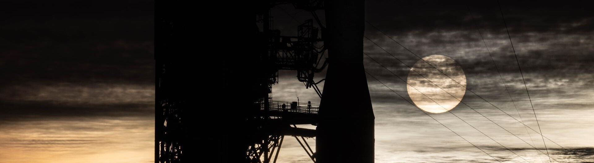 Sonnenaufgang am Kennedy Space Center in Florida: Die Sonne ist hinter dem Raketenkopf von Artemis II zu sehen. Am Himmel sind Schleierwolken zu sehen.A