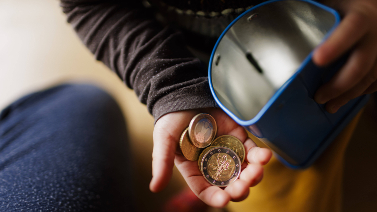 Geldmünzen in einer Kinderhand und eine Blechdose