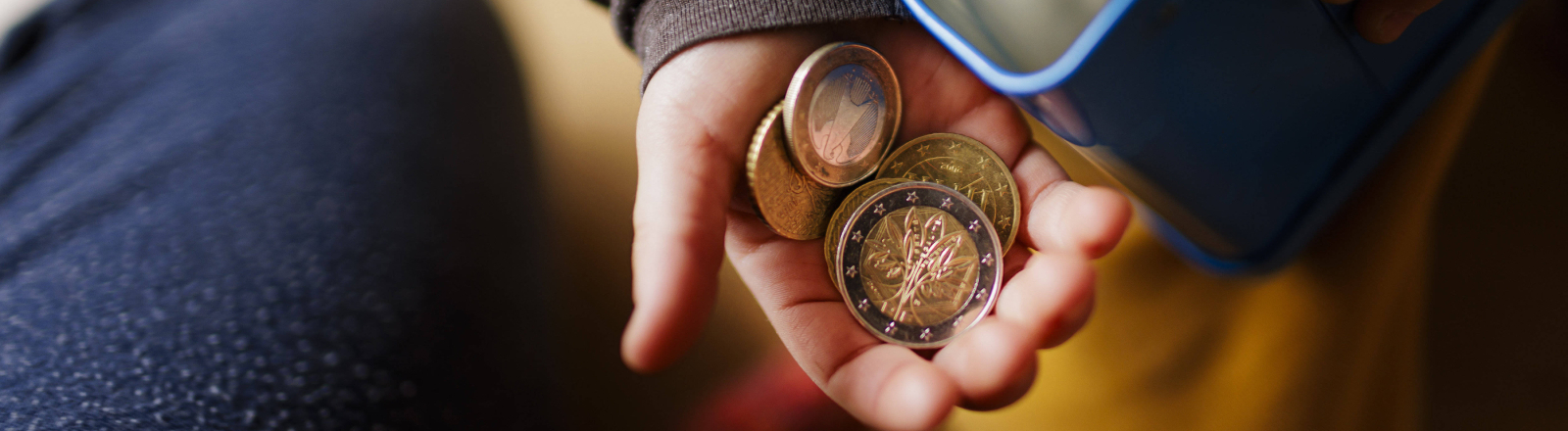 Geldmünzen in einer Kinderhand und eine Blechdose