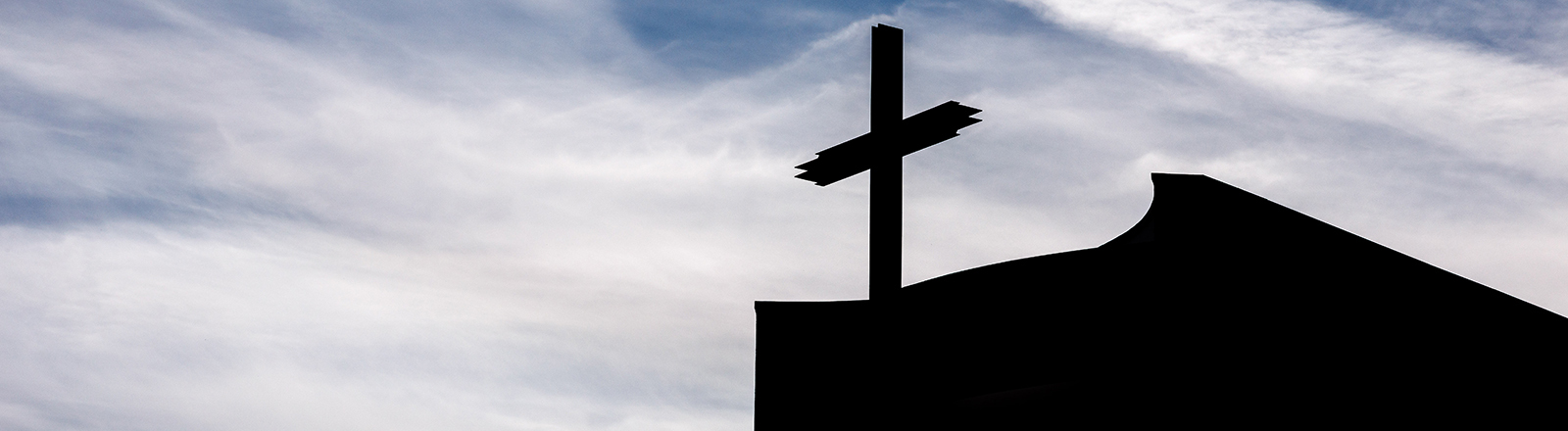 Ein Kreuz auf einer Kirche im Gegenlicht
