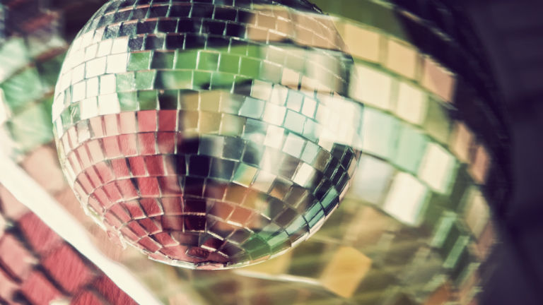 Eine Diskokugel schillert im bunten Licht.