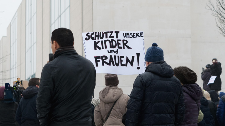 Demonstranten stehen am 23.01.2016 in Berlin vor dem Kanzleramt mit einem Schild, auf dem "Schützt unsere Kinder und Frauen" zu lesen ist. Die Proteste beziehen sich auf Gerüchte zu einer angeblichen Vergewaltigung einer Minderjährigen aus einer deutsch-russischen Familie im Berliner Bezirk Marzahn-Hellersdorf. Die Faktenlage zu dem Vorfall, der auch in den sozialen Netzwerken eine Rolle spielt, ist noch weitgehend unklar. Laut Polizeiangaben habe es weder eine Entführung noch eine Vergewaltigung gegeben.