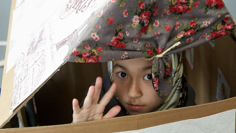 Ein Kind sitzt in einem Haus aus Pappe.