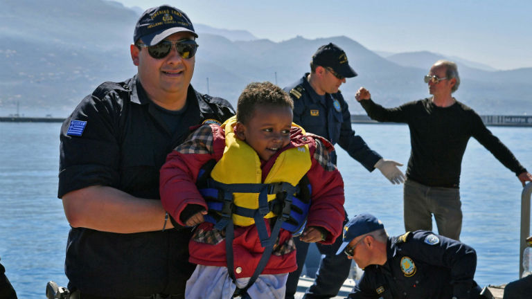 Ein griechischer Helfer mit einem geretteten kleinen Jungen in Schwimmweste.