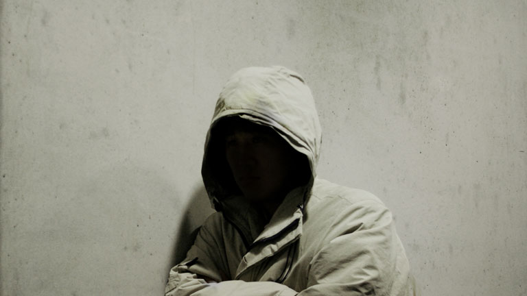 Unbekannter Kapuzentyp lehnt an einer Mauer