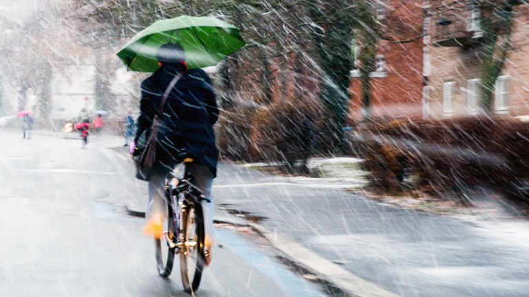 Ein Fahrradfahrer mit Regenschirm in der Hand fährt am 13.01.2017 in Göttingen (Niedersachsen) durch den Schneeregen.