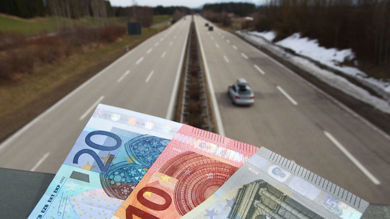 Verschiedene Euro-Banknoten liegen auf dem Geländer einer Autobahnbrücke