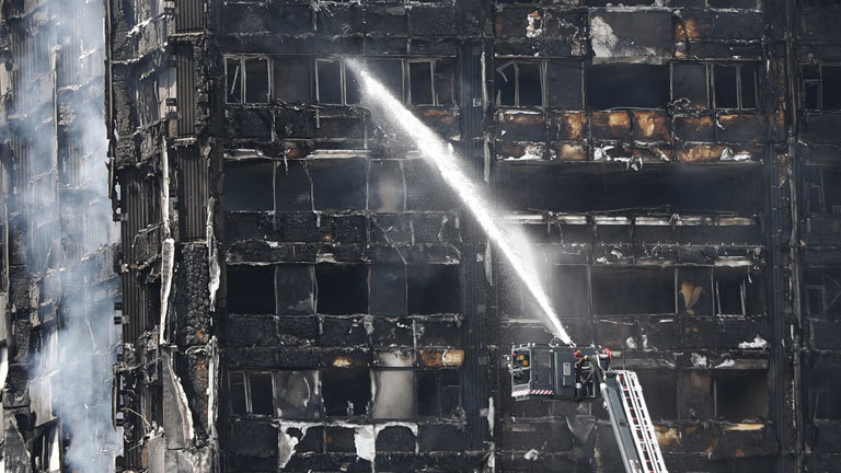 Feuerwehrleute spritzen am 14.06.2017 in London (Großbritannien) Wasser auf das noch rauchende Hochhaus. Bei dem Brand eines Hochhauses im Zentrum Londons sind mehrere Menschen ums Leben gekommen. Das Feuer war in der Nacht ausgebrochen, am frühen Morgen stand das Gebäude mit mehr als 20 Stockwerken noch lichterloh in Flammen.