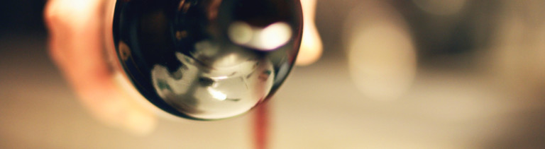 Eine Hand gießt Rotwein aus einer Glasflasche.