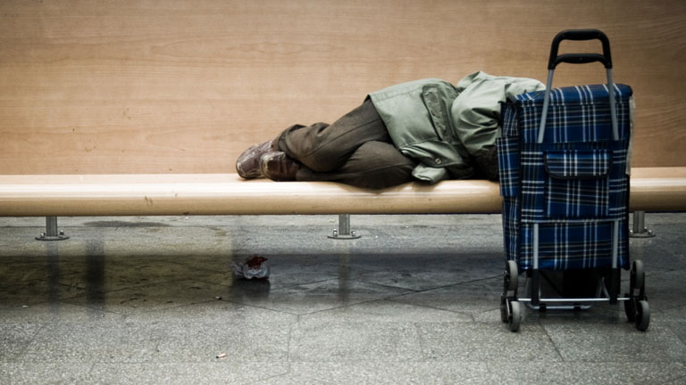 Ein armer Mann schläft auf einer Bank.