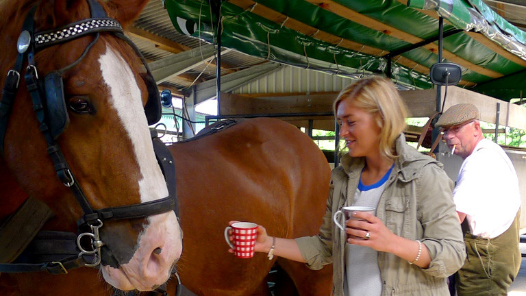 Anne Bente Isenburg mit zwei Tassen Kaffee vor einem Pferd.