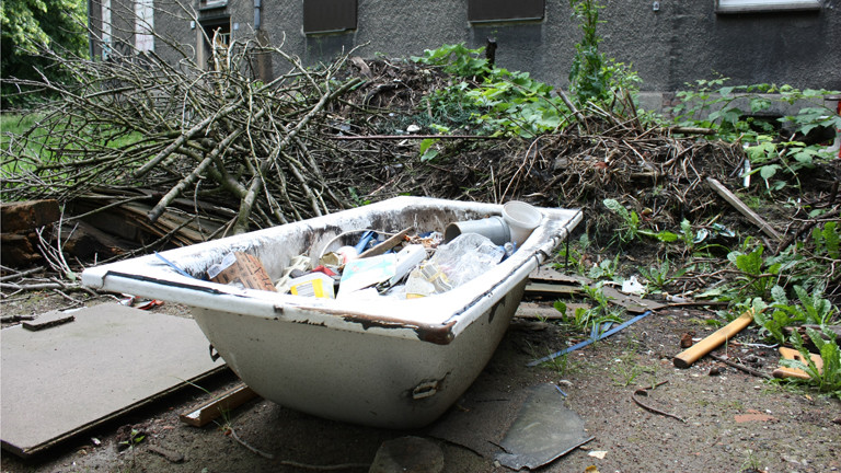 Eine alte Badewanne steht voller Müll im Hof.