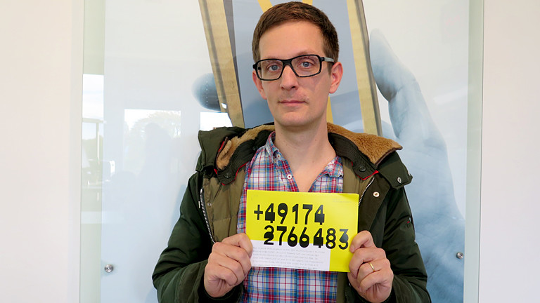Ein Mann hält einen Zettel mit einer Handynummer