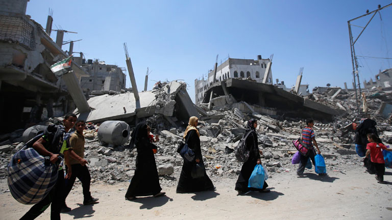 Menschen im Gazastreifen tragen ihr Hab und Gut an einem zerstörten Haus vorbei.