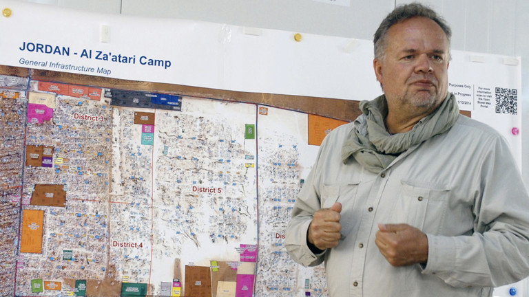 Kilian Kleinschmidt vor einer Wand mit Plänen vom Flüchtlingslager.