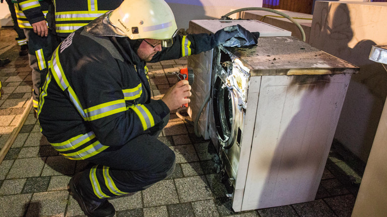 Ein Feuerwehrmann begutachtet einen ausgebrannten Wäschetrockner