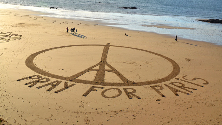 In den Sand an einem Strand ist ein Peace-Symbol mit Eiffelturm gemalt. Dazu die Worte "Pray for Paris".