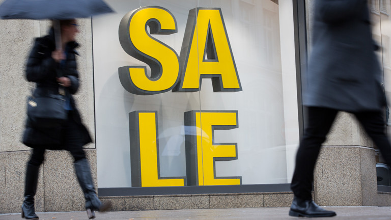 Menschen laufen an einem Sale-Schild vorbei.