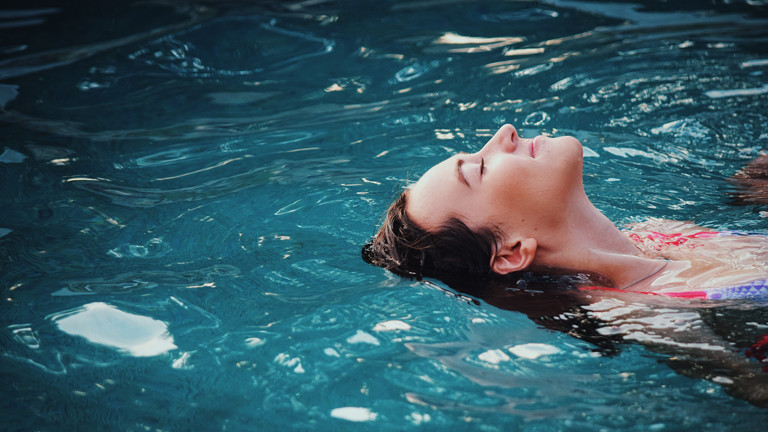 Frau liegt mit geschlossenen Augen auf dem Rücken in einem Swimmingpool.