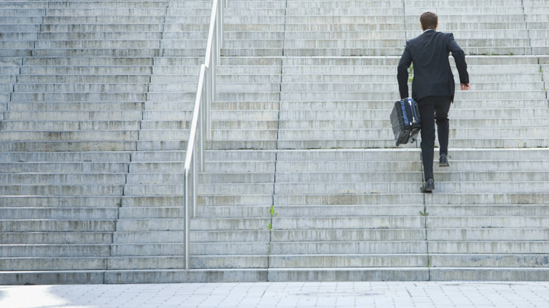 Mann im Anzug rennt mit Koffer eine Treppe hinauf