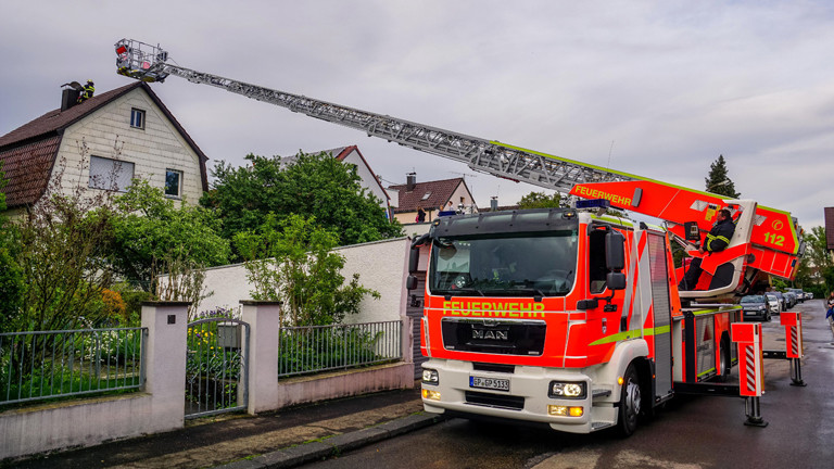 Ein Feuerwehrauto vor einem Wohnhaus, die Drehleiter ist zum Dach hin ausgefahren.