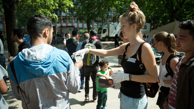 Eine Helferin verteilt Essen und Getränke am Berliner Landesamt für Gesundheit und Soziales