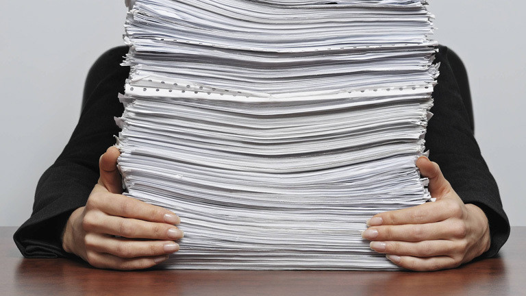 Person hinter einem Papierstapel
