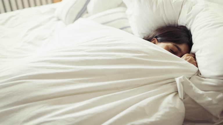 Frau liegt im bett und zieht die Decke bis zur Nasenspitze
