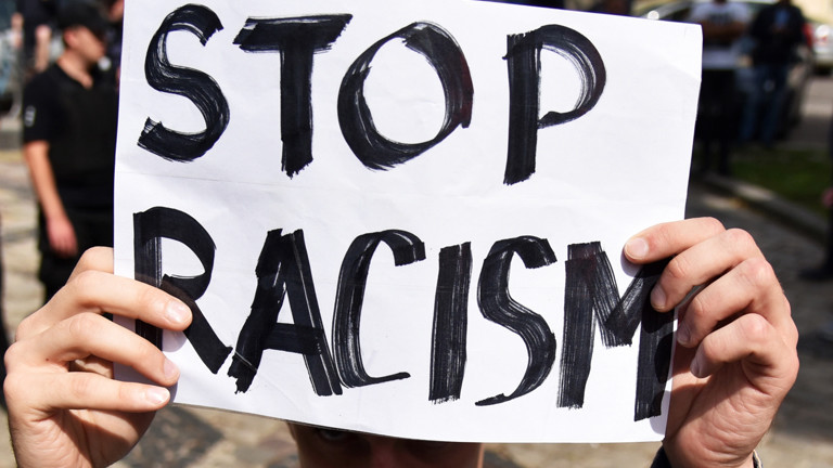 zwei Hände halten einen Zettel: Stop Racism