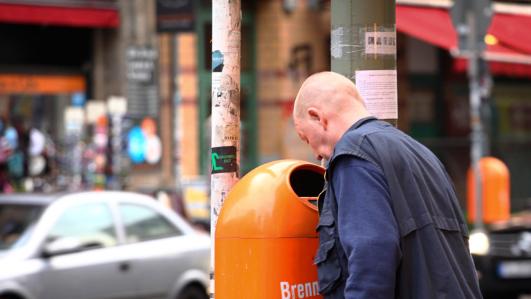 Ein Mann schaut in eine orange Mülltonne