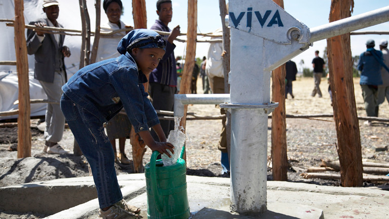 Ein kleines Mädchen steht in Afrika an einem Brunnen und füllt Trinkwasser in eine Plastikflasche.