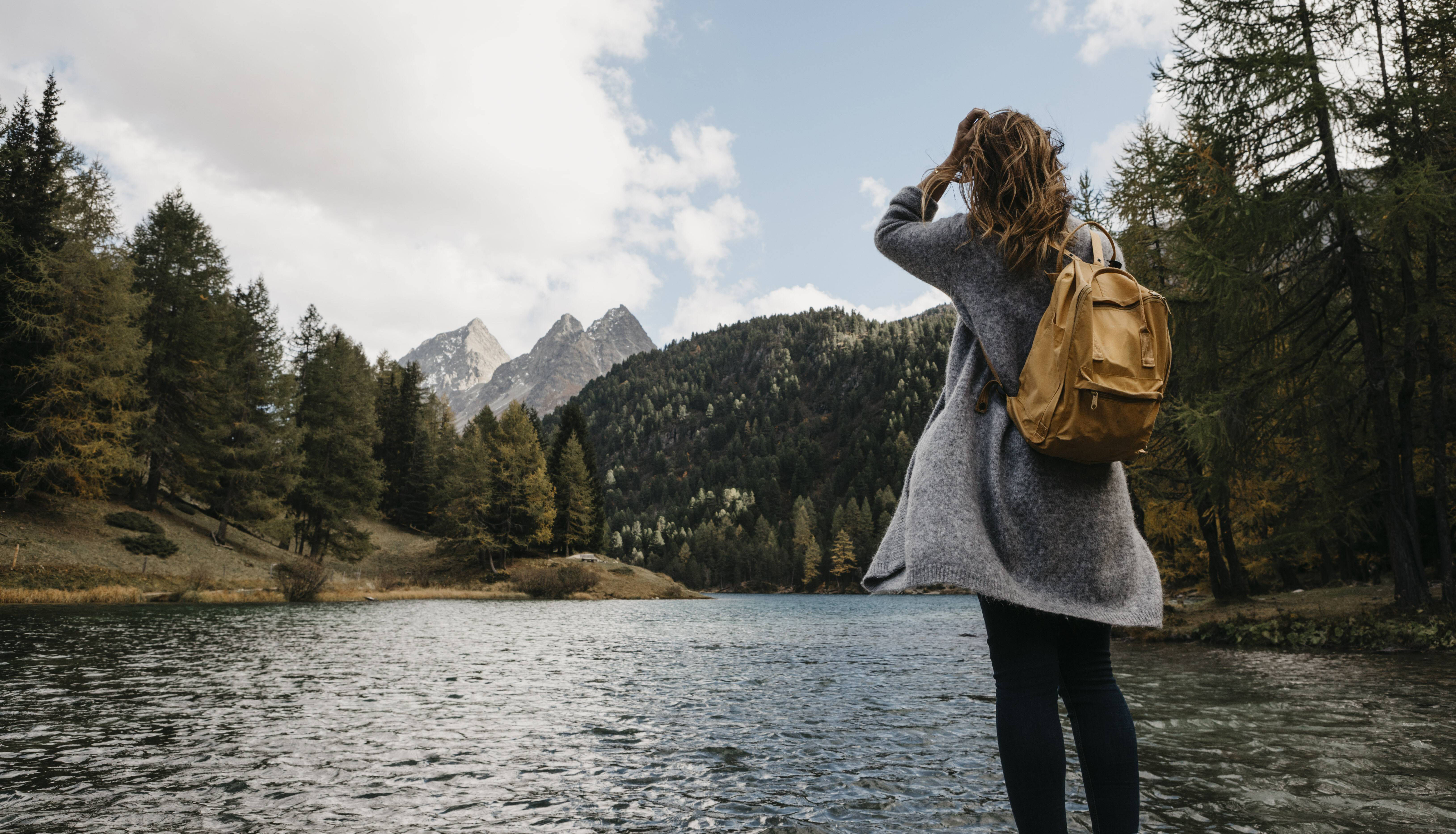 Frau steht in den Bergen an einem Waldsee.