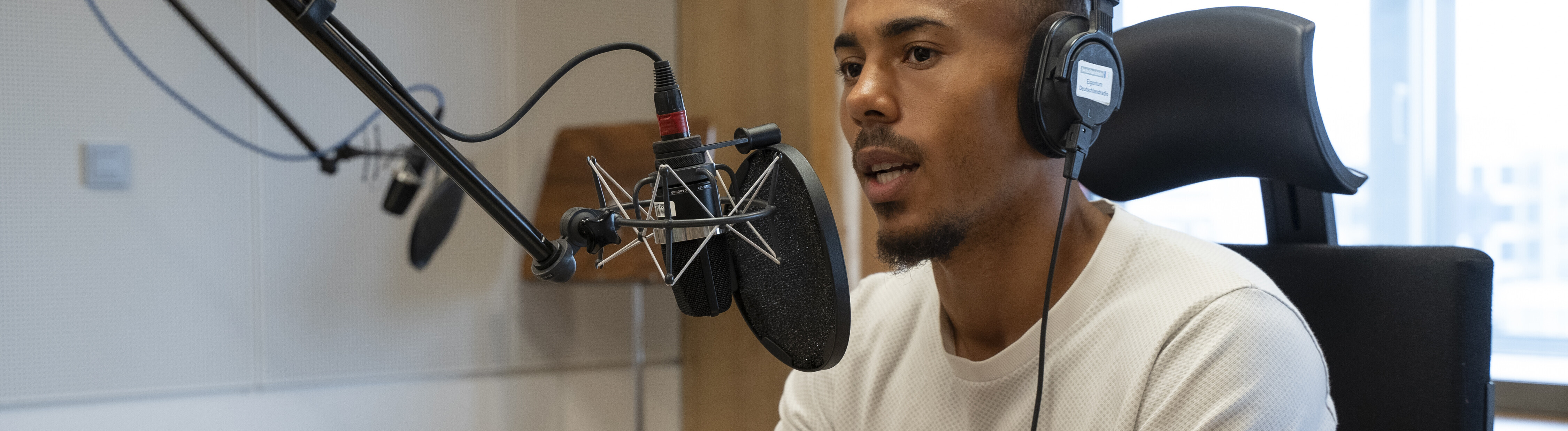 Der Fußballspieler Robin Afamefuna sitzt im Dlf Nova-Studio am Mikrofon und hat einen Kopfhörer auf.