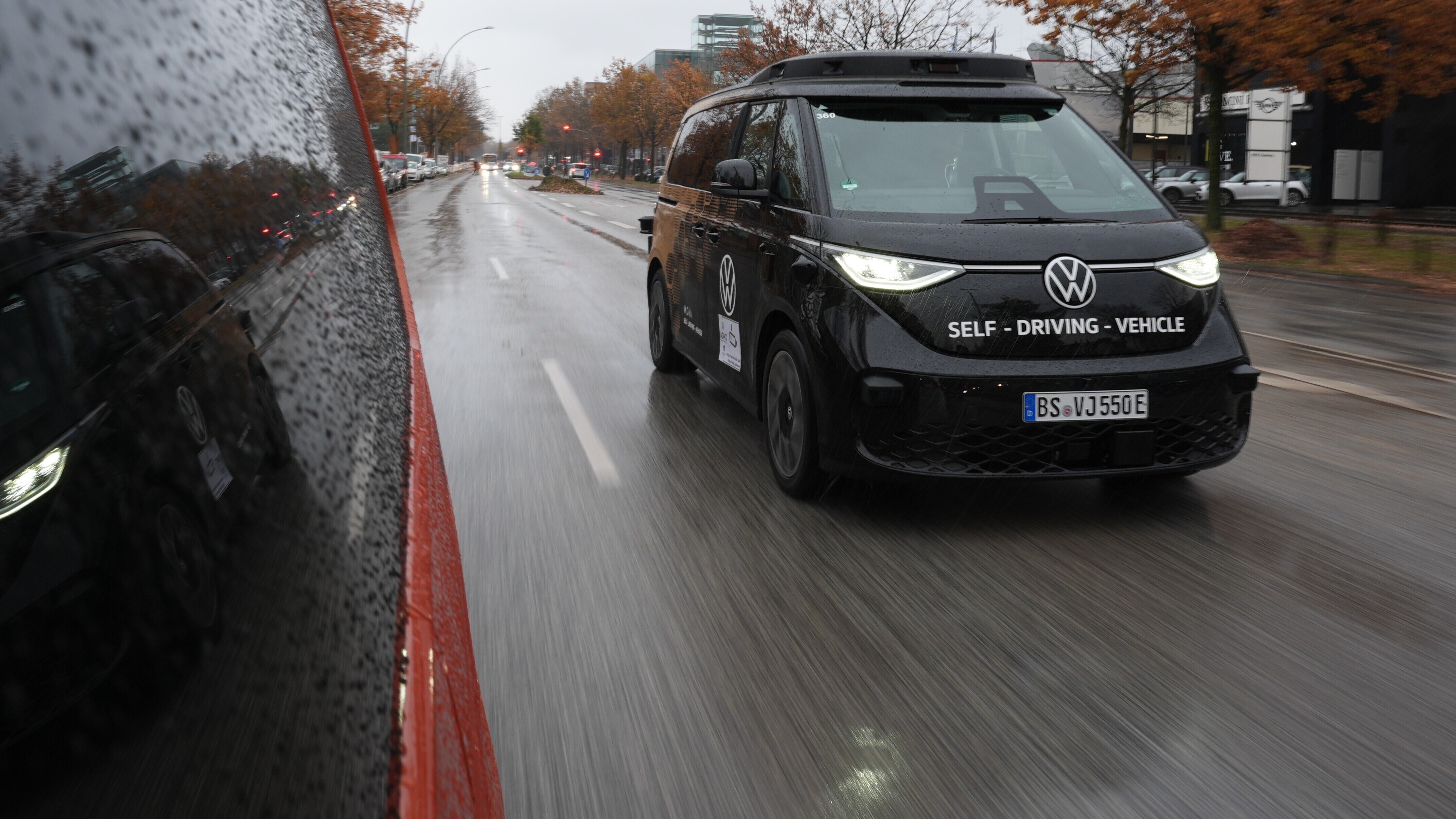 Ein schwarzer Kleinbus der Marke VW fährt auf einer Straße. Vorne auf dem Kleinbus steht "Self Driving Vehicle". Der Kleinbus fährt autonom, also ohne Fahrer. Diese Modelle werden in Hamburg getestet.