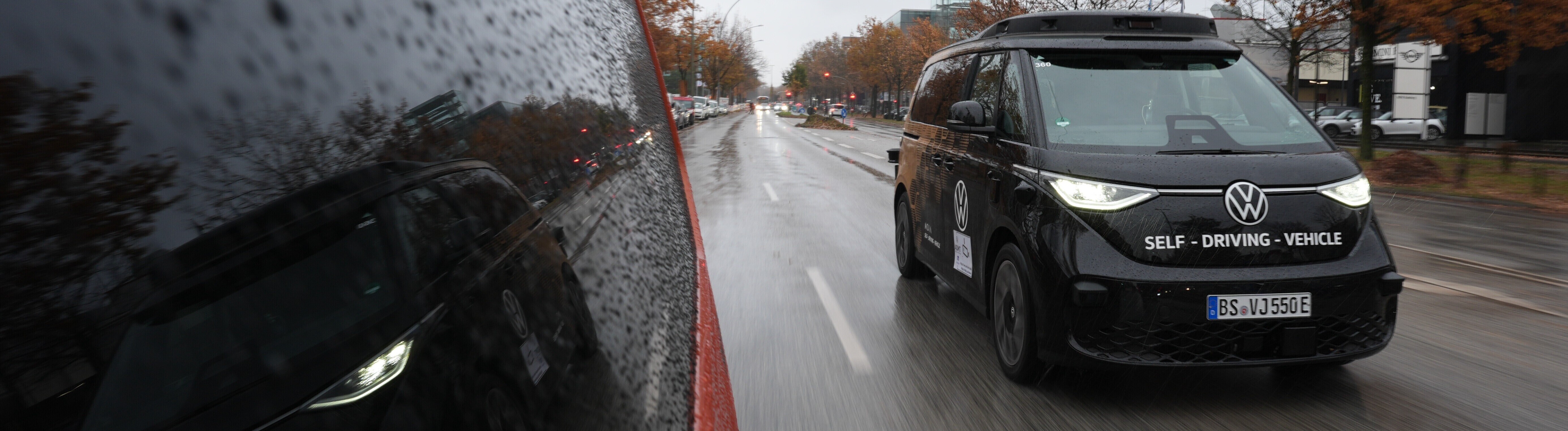Ein schwarzer Kleinbus der Marke VW fährt auf einer Straße. Vorne auf dem Kleinbus steht "Self Driving Vehicle". Der Kleinbus fährt autonom, also ohne Fahrer. Diese Modelle werden in Hamburg getestet.