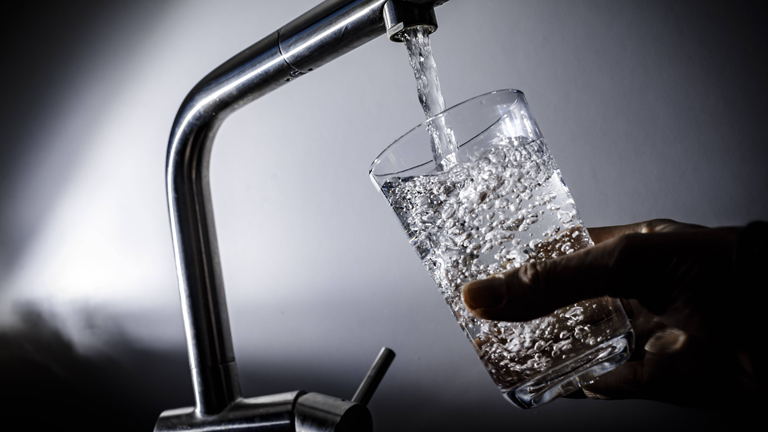 Ein Glas wird unter einer Wasserleitung aufgefüllt