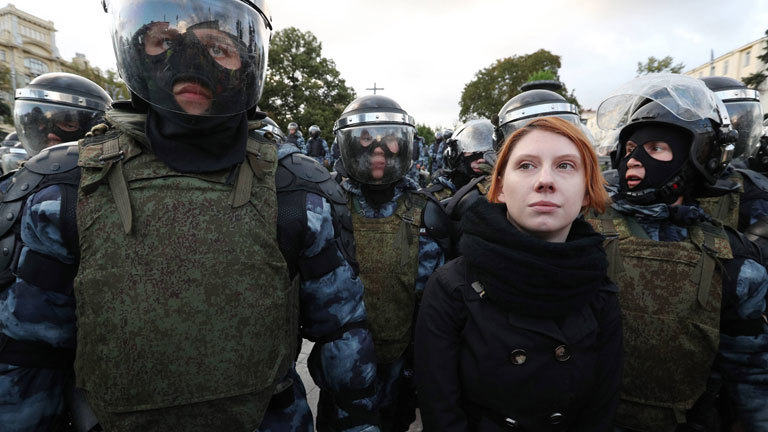 Bei einer Demonstration in Moskau steht eine junge Frau zwischen Polizisten. 10. August 2019.