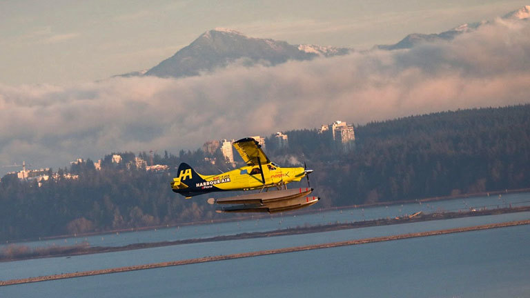 Das erste kommerzielle E-Flugzeug startet; es ist ein Wasserflugzeug mit E-Motor. Der Flug ist in Kanada, im Hintergrund verschneite Berge.