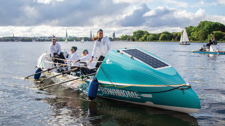 Auf einem modernen Ruderboot sitzen vier Frauen; sie rudern auf der Alster. Demnächst wollen sie den Atlantik überqueren.