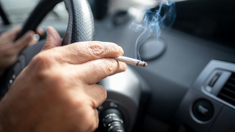 Ein Mann sitzt rauchend am Lenkrad eines Autos