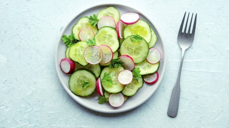 Auf einem Teller liegt ein Salat bestehend aus Gurkenscheiben, Radieschen und Petersilie. Neben dem Teller liegt eine Gabel.