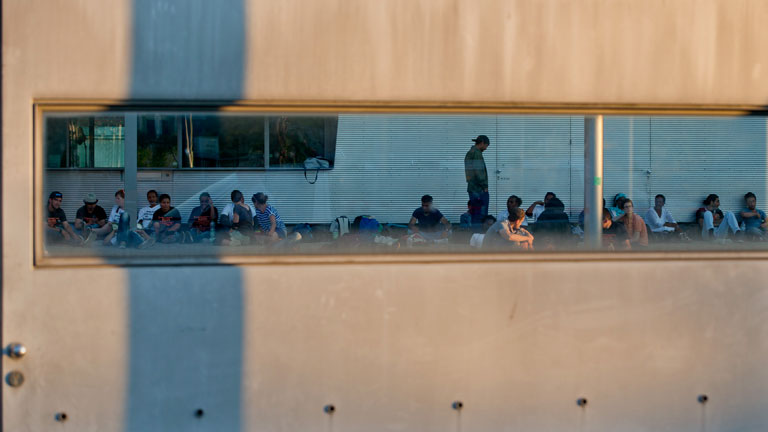 Flüchtlinge sitzen in einem Hof des Bundesamts für Migration und Flüchtlinge. Sie wurden durch eine Tür fotografiert.