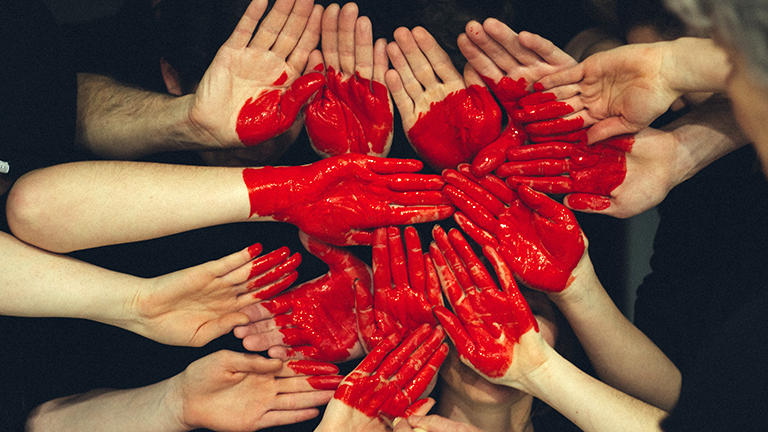 Viele Hände zeigen in die Kamera auf die ein großes rotes Herz gemalt ist