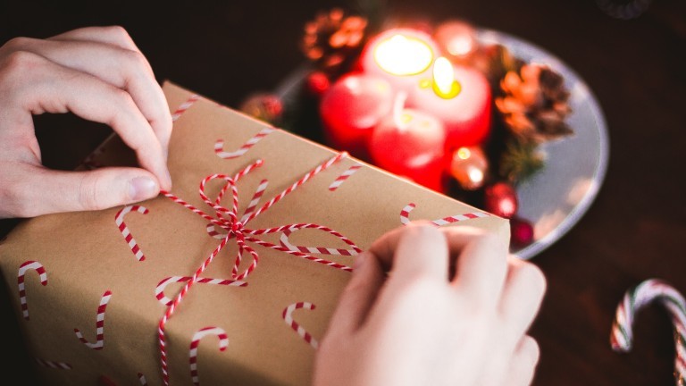Eine Person verpackt ein Weihnachtsgeschenk an einem Tisch. Davor ist ein Adventskranz.