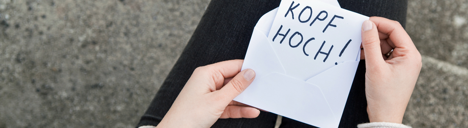 Eine Frau hält einen Zettel in den Händen: "Kopf hoch".