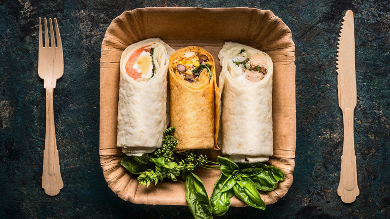 Frische Wraps auf Pappteller mit Holzbesteck daneben